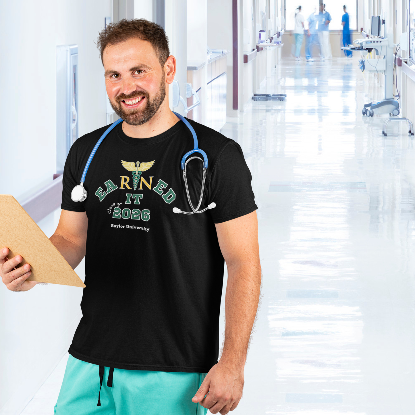 Person wearing a black t-shirt with 'Earned It 2026' text, holding a stethoscope in a hospital setting.